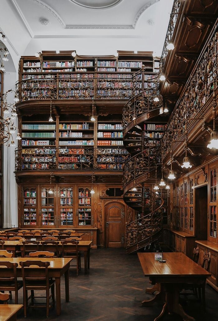 Grandioso interno di biblioteca con scaffali in legno, scala a chiocciola e accoglienti tavoli da lettura pieni di libri da tutto il mondo.
